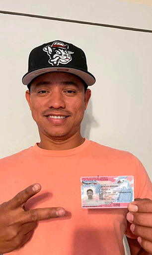 Hombre inmigrante sonriendo y haciendo señal de victoria mientras sostiene su tarjeta de permiso de trabajo de inmigración