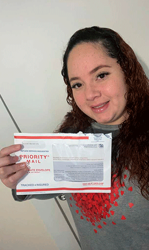 “Mujer inmigrante sonriendo mientras sostiene un sobre de Priority Mail de USCIS recibido en casa”
